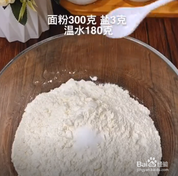 碗中加入300克面粉,三克食盐,用180克的温水把它搅拌成絮状,再揉成